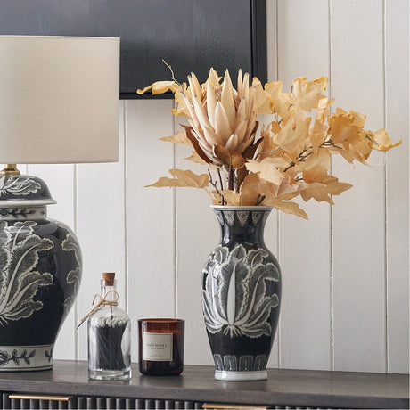 Black & White Feather Ceramic Urn Vase, 31cm, with dried floral stems on a dark sideboard beside a patterned lamp and candle.