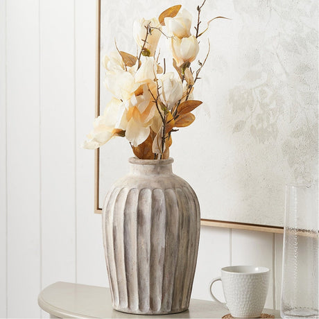 Ambrosia Natural Grooved Stoneware Vase, 30cm, with ridged texture holding cream floral stems, styled on a table beside a mug and glass vase.