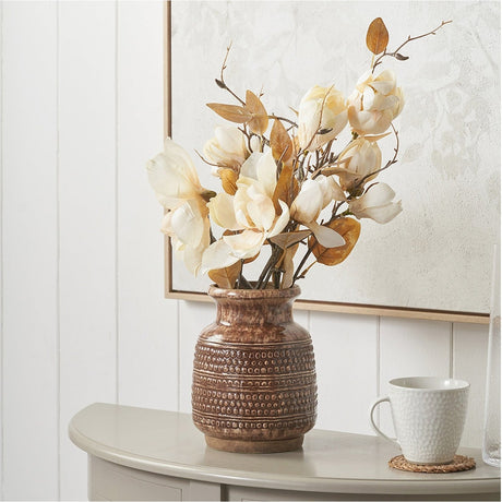 Theano Dot Design Brown Glaze Vase, 20cm ceramic vase with textured dot pattern, holding cream faux flowers on a console table beside a white mug.