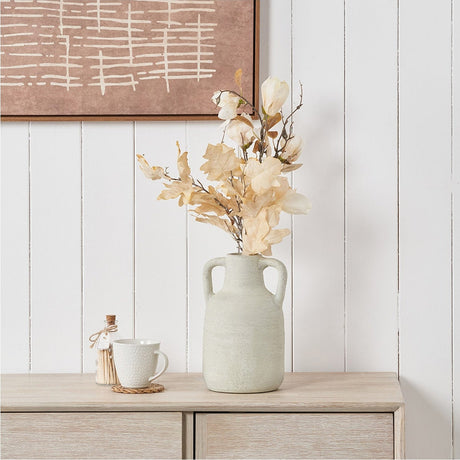 White textured terracotta medium vase with handles holding dried florals on a wooden sideboard, styled with a mug and matchbox against panelled walls.
