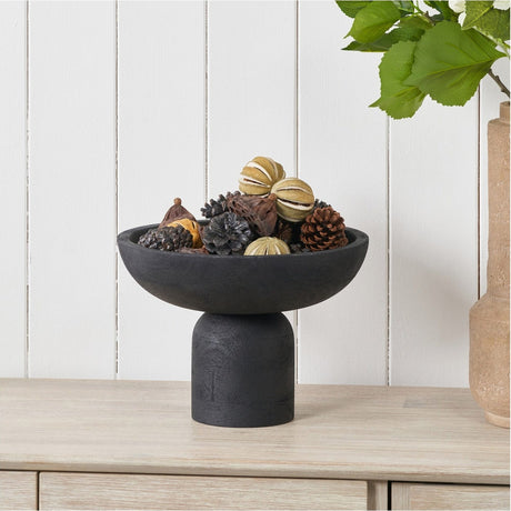 Black handcarved mango wood bowl, 29cm, with raised pedestal base, filled with pinecones and dried fruit, styled on a sideboard.