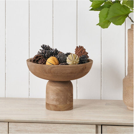 Natural handcarved mango wood bowl, 29cm, with raised pedestal base, shown filled with pinecones and decorative gourds on a wooden sideboard.