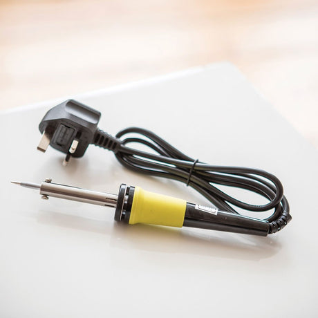 AVSL Mercury 30W mains soldering iron with yellow grip, stainless barrel, coiled black lead and UK plug, resting on a white surface.