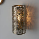 Endon Cliffmere wall light in antique brass, cylindrical steel shade with cut-out secret-garden design of leaves and birds, casting patterned glow on wall.