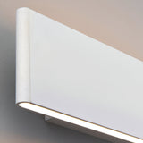 Close-up of the Endon Ambrose matt white LED wall light showing its slim rectangular form, rounded end cap and warm downward glow against a pale wall.