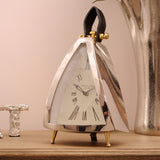 Libra Interiors Polished Nickel Curved Front Mantel Clock with cream roman numeral dial, black leather loop handle and brass feet on a wooden sideboard.
