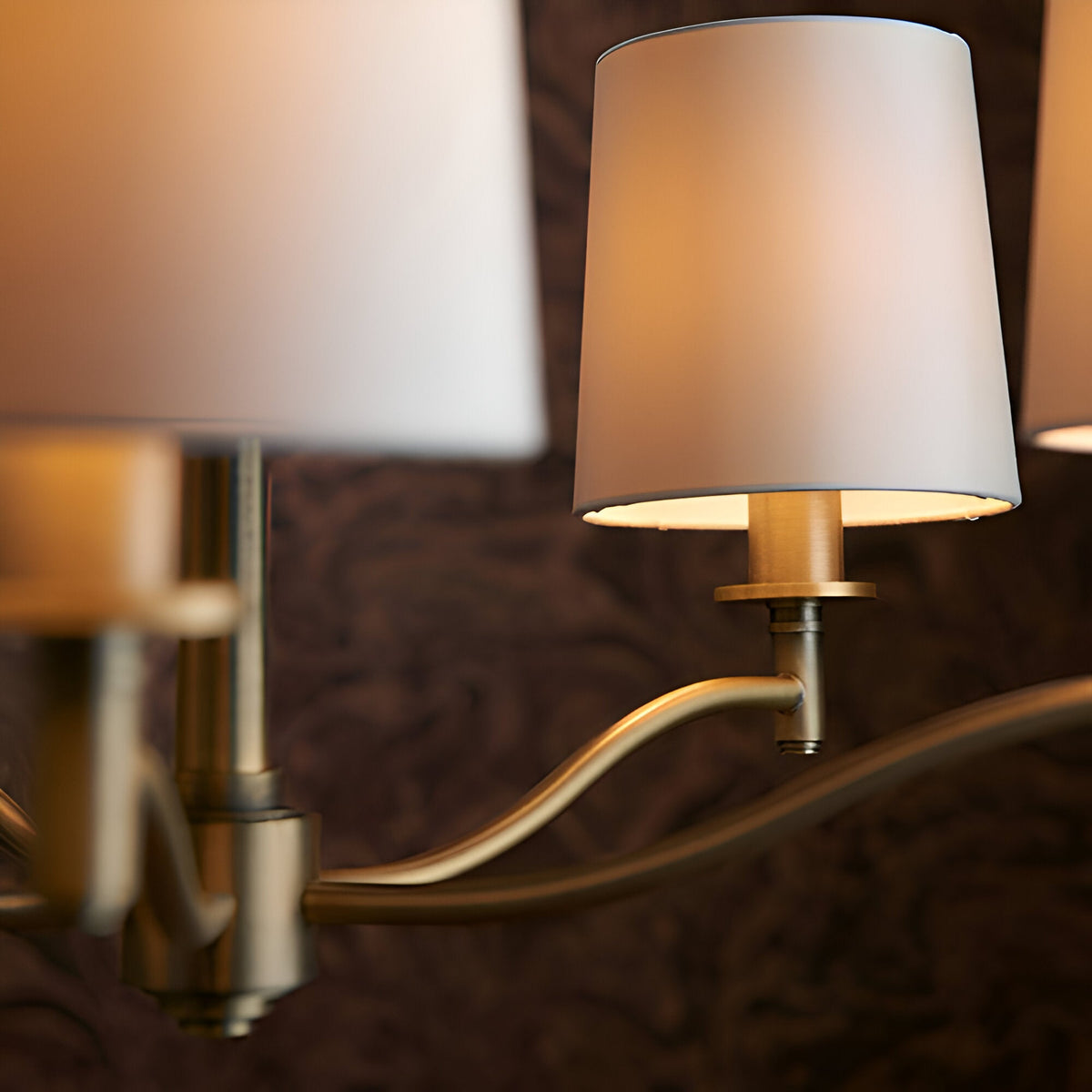 Close-up of Endon Castwell pendant arm in matt antique brass with a vintage white faux silk shade, warmly lit against a dark backdrop.
