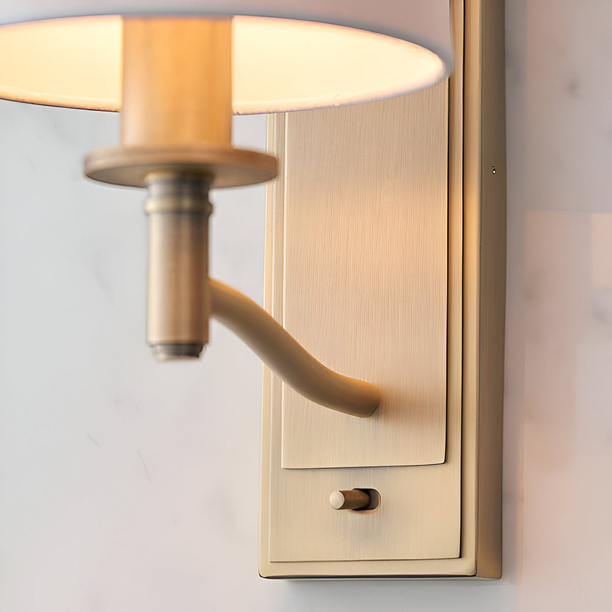 Close-up of Endon Castwell wall light in matt antique brass, showing the curved arm, toggle switch, and base of the vintage white faux-silk shade.