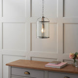 Endon Caldbury pendant light in nickel with clear glass panels and chain suspension, hung above a grey sideboard against a panelled wall.