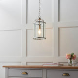 Endon Caldbury pendant light in nickel with clear glass panels and E27 filament lamp, hung from a chain above a grey sideboard in a panelled room.