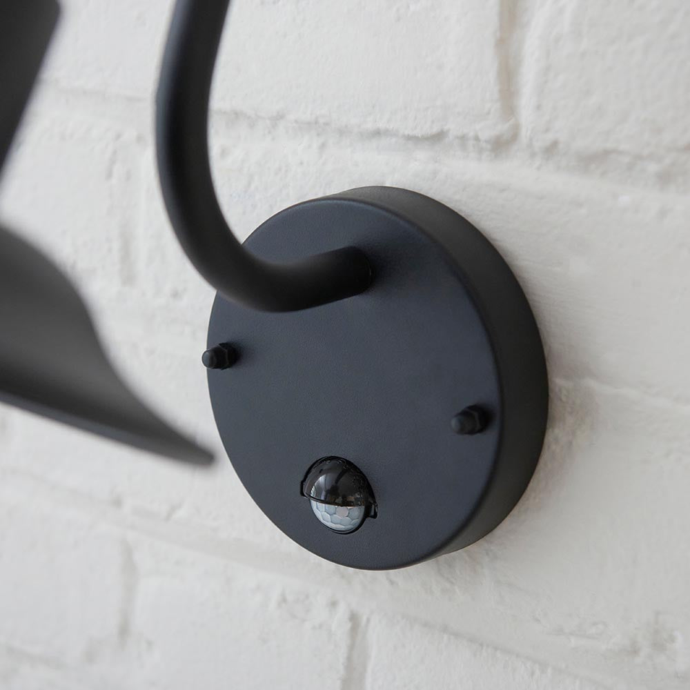 Close-up of the Endon Bevfield PIR outdoor wall light in textured black, showing the circular wall plate and built-in motion sensor on white brick.