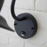 Close-up of the Endon Bevfield PIR outdoor wall light in textured black, showing the circular wall plate and built-in motion sensor on white brick.