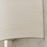 Close-up of the Endon Castmere wall light's semi-circular white linen shade, showing the woven fabric texture and curved lower edge against a pale wall.
