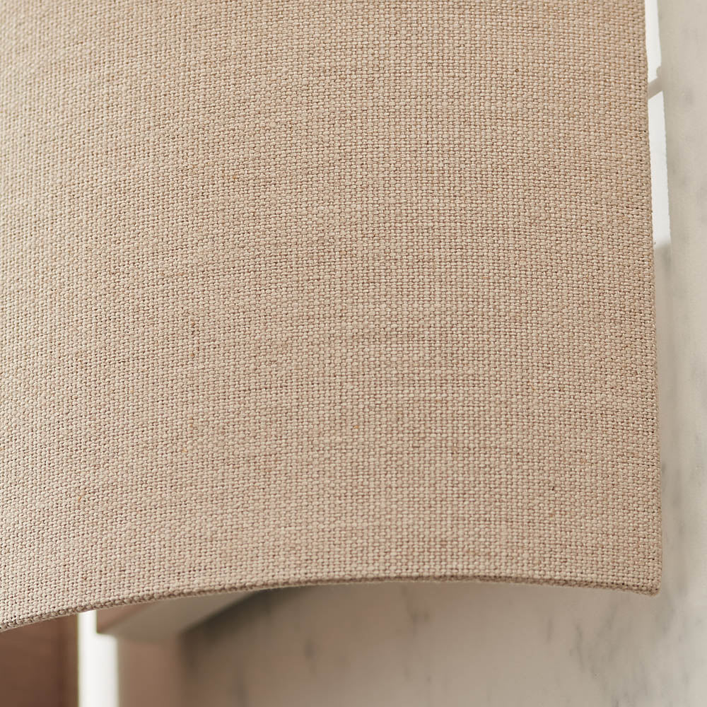 Close-up of the Endon Castmere wall light in natural linen, showing the semi-circular fabric shade and steel frame mounted on a pale wall.