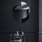 Libra Interiors Overlapping Circles wall mirror in clear and black glass, mounted on a dark panelled wall above a chrome and glass drinks trolley.