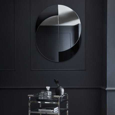 Libra Interiors Overlapping Circles wall mirror in clear and black glass, mounted on a dark panelled wall above a chrome and glass drinks trolley.