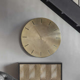 Libra Interiors Brushed Gold Iron Round Wall Clock with raised hour markers and slim hands, mounted on a grey wall above a patterned gold sideboard.