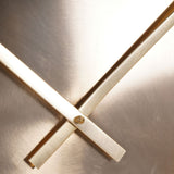 Close-up of Libra Interiors Brushed Gold Iron Round Wall Clock showing slim metallic hands crossed at a brass centre screw on the warm gold dial.