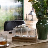 Libra Interiors Glass & Ribbed Wood Candle Holder with three lit votives in a grooved wooden base, styled on a dining table beside a green vase of eucalyptus.