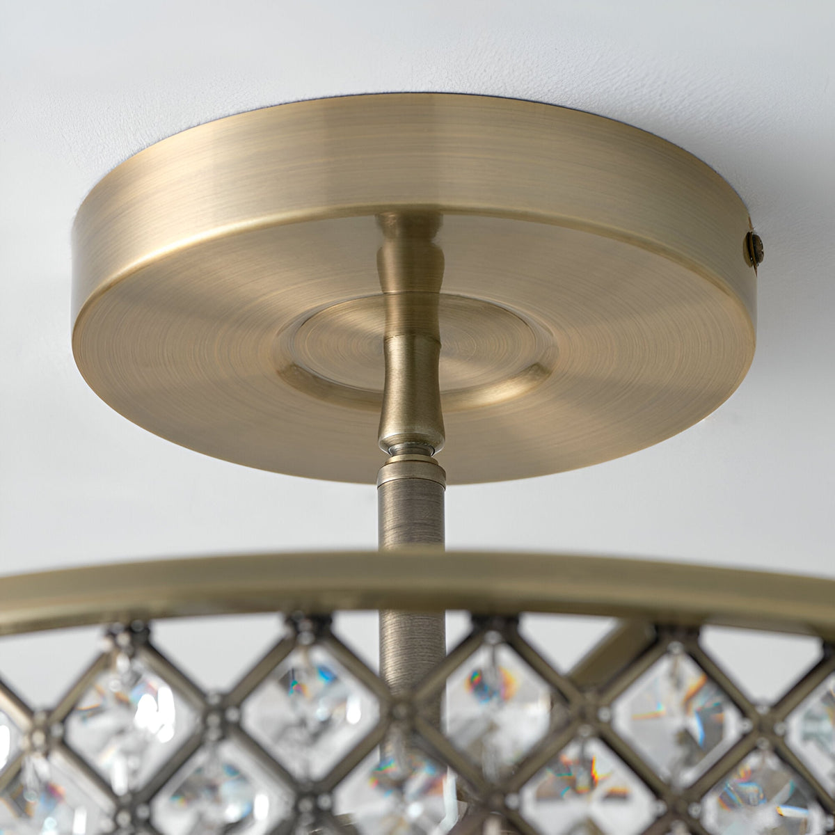 Close-up of Endon Prescott 3 Light flush ceiling light showing antique brass ceiling plate, stem, and crystal-set frame edge against a white ceiling.