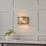 Endon Prescott two-light wall fitting in antique brass with crystal beads, mounted on a panelled wall above a marble console with a fern and books.
