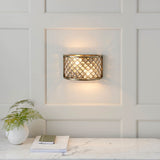 Endon Prescott antique brass wall light with crystal beads in a steel frame, illuminated on a panelled wall above a marble console with a fern and books.