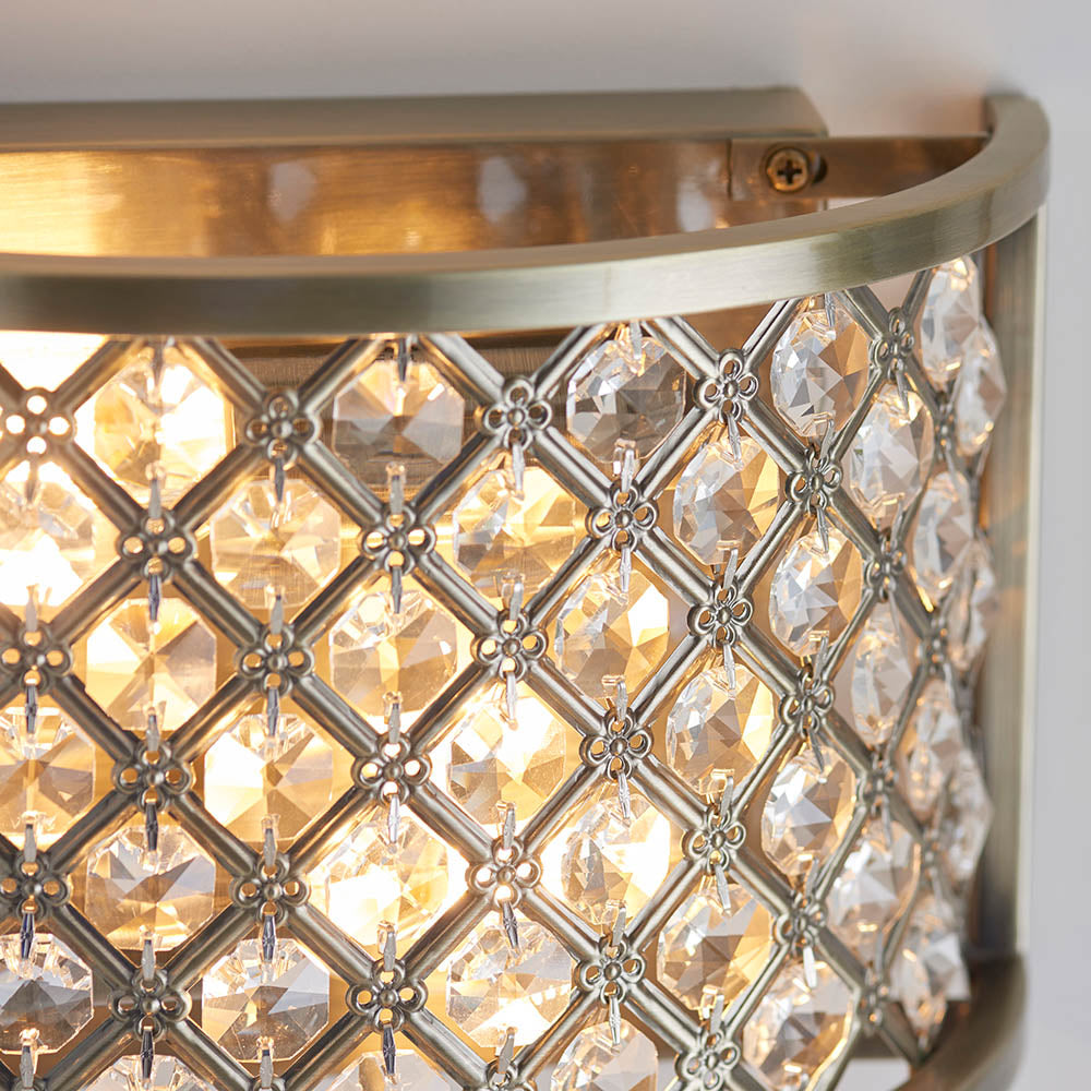 Close-up of the Endon Prescott antique brass wall light showing the crystal bead lattice and curved steel frame illuminated with a warm glow.