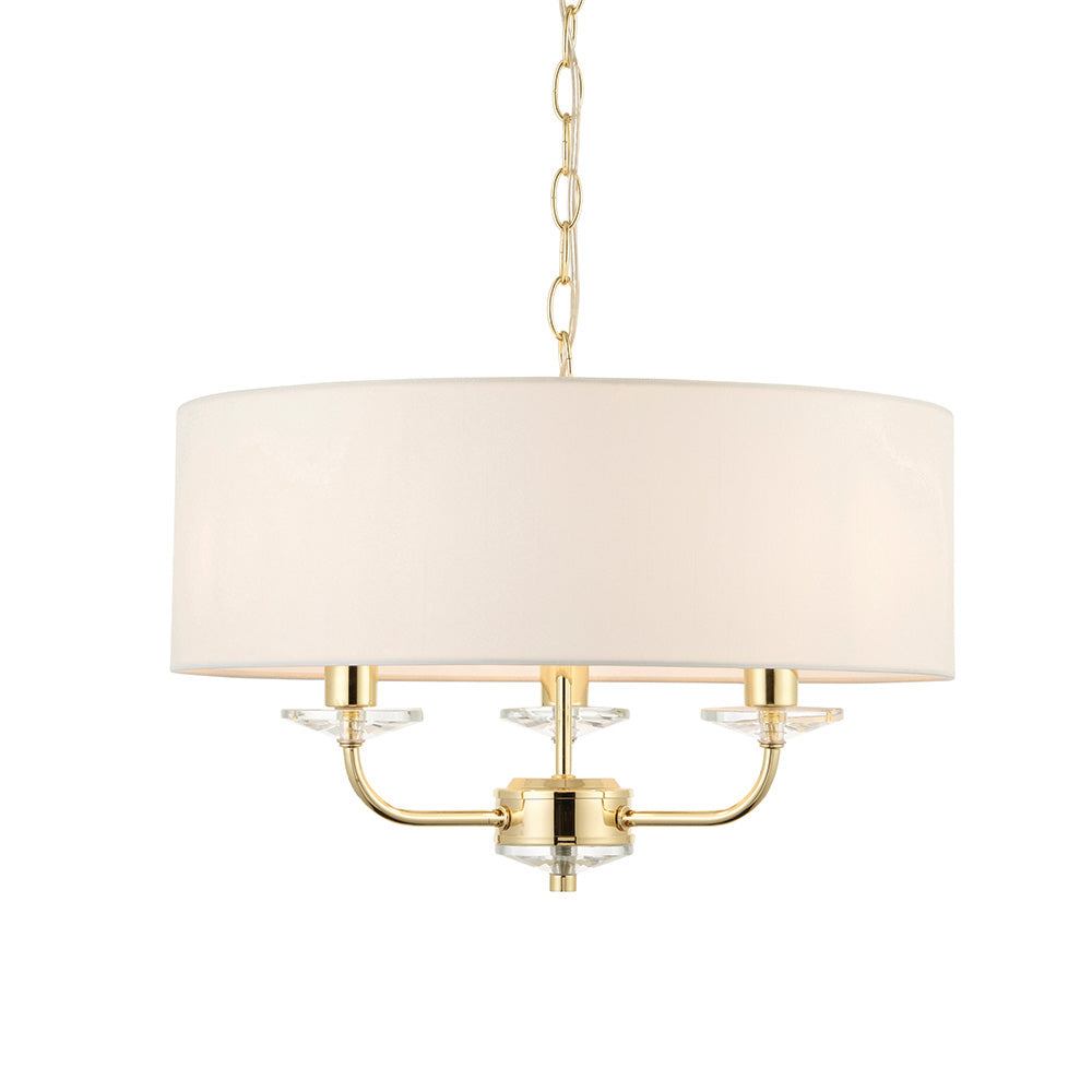 Endon Castdon 3 light pendant in brass with a wide white faux silk drum shade, three arms with K9 crystal detail, and suspension chain, on white.