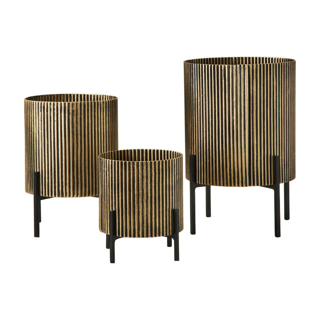 Libra Interiors Ribbed Iron Set of 3 Footed Planters in antique gold with ebony shading, graduated cylindrical bodies on slim black legs, on a white background.