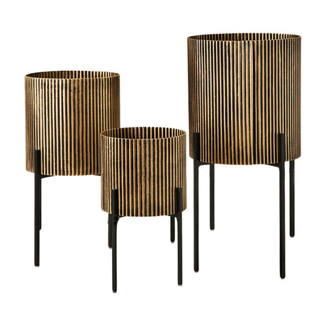 Libra Interiors Ribbed Iron Set of 3 Standing Planters in antique gold with ebony detailing, raised on tapered black iron legs, on a white background.