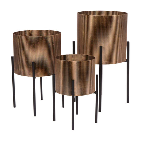 Libra Interiors Ribbed Iron Set of 3 Standing Planters in antique gold, cylindrical fluted bodies on tapered black iron legs, shown on a white background.