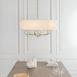 Endon Castdon 6 light pendant in brass with white drum shade and K9 crystal detail, suspended above a wooden dining table in a panelled room.