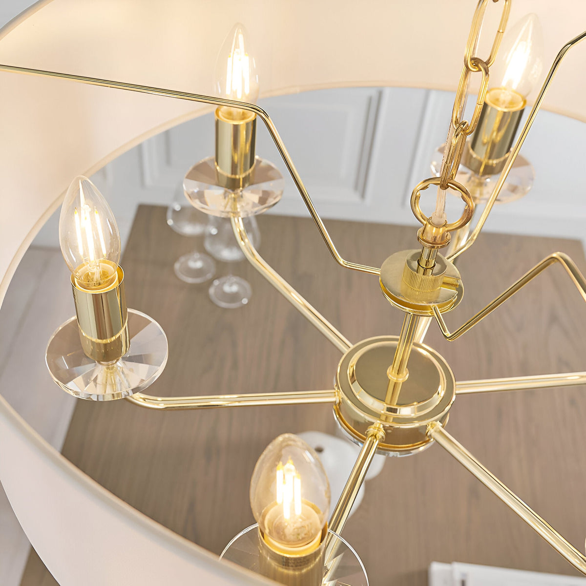 Close-up of Endon Castdon 6 light pendant showing brass arms, K9 crystal bobeches, E14 candle bulbs and chain suspension above a wooden dining table.