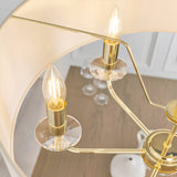 Close-up of the Endon Castdon 6 Light Pendant showing brass arms with K9 crystal bobeches, E14 candle bulbs and white faux silk shades above a dining table.