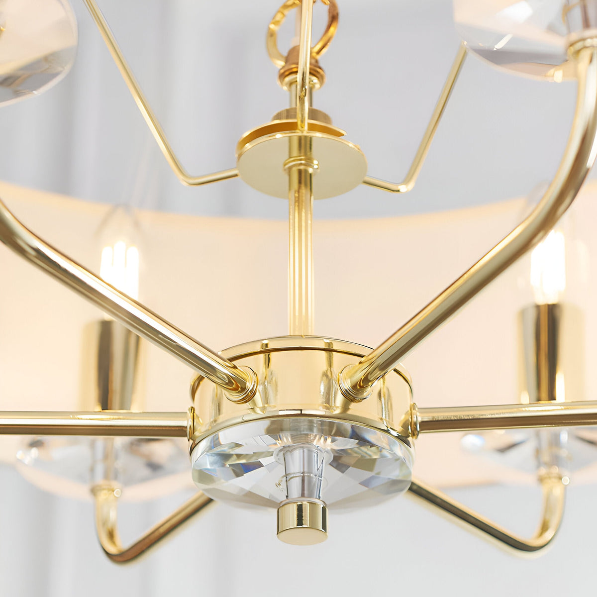 Close-up of the Endon Castdon 6 Light Pendant showing the polished brass arms, central K9 crystal detail, and chain suspension beneath white shades.