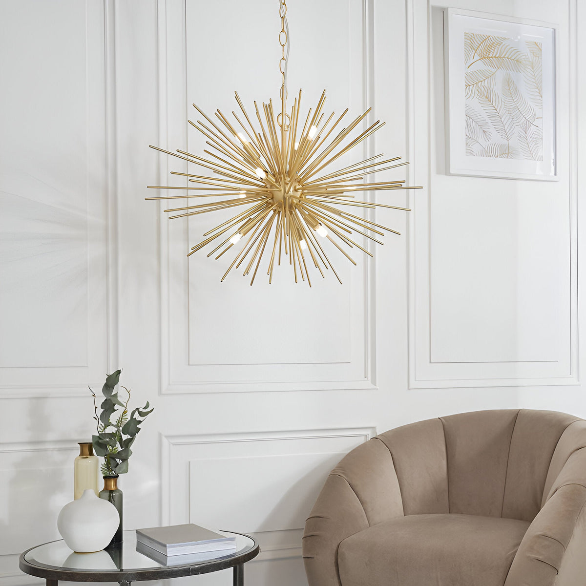 Merrick 9 Light Sputnik Pendant in satin brass, star-burst arrangement of metal rods with exposed bulbs on a chain, hanging in a living room above a chair and side table.