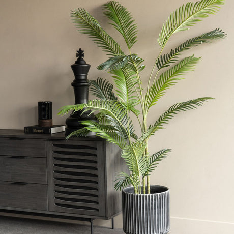 Libra Interiors Faux Areca Palm 6ft in a ribbed grey planter beside a dark wood sideboard with a black chess king ornament and Monet book.