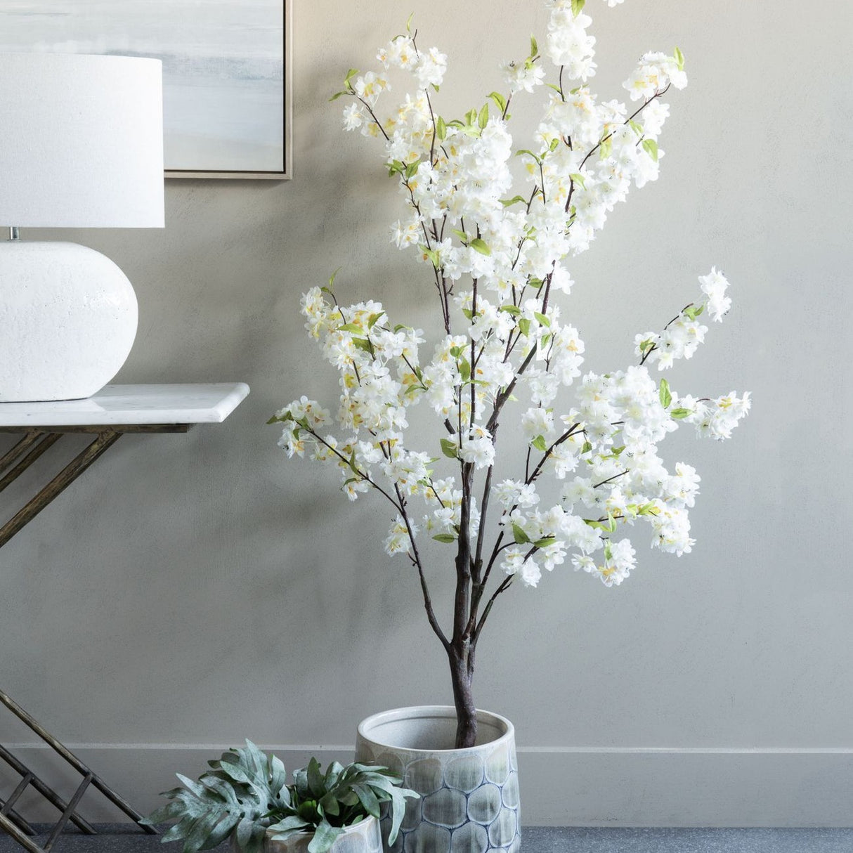 Libra Interiors Potted White Blossom Cherry artificial tree with slim brown branches and green leaves, styled beside a console table with lamp.