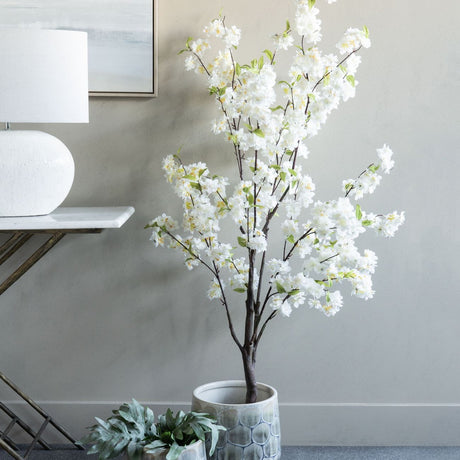 Libra Interiors Potted White Blossom Cherry artificial tree with slim brown branches and green leaves, styled beside a console table with lamp.