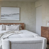 Libra Interiors Textured Boucle Storage Ottoman in cream, placed at the foot of a wooden bed with white bedding, beside a wood dresser in a neutral bedroom.