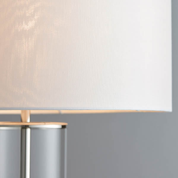 Close-up of the Endon Caldley table lamp showing its white faux silk drum shade meeting the nickel fitting and clear cylindrical glass base.