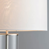 Close-up of the Endon Caldley table lamp showing its white faux silk drum shade meeting the nickel fitting and clear cylindrical glass base.