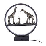 Libra Interiors LED Giraffe Family light in bronze, featuring two adults and a resting calf inside a matt black LED ring on a square base.