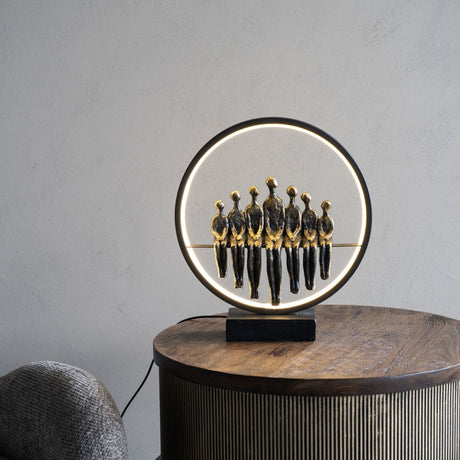 Libra Interiors Bronze Family Circle LED lighting accessory with seven resin figures inside a black illuminated ring, displayed on a round wooden side table.