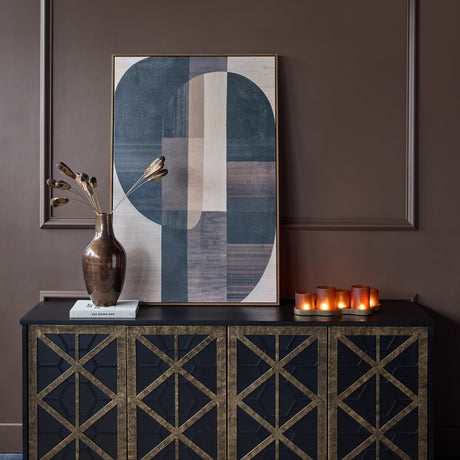 Libra Interiors Fretwork black mango wood sideboard styled in a moody interior with abstract geometric art, bronze vase and lit candles on top.