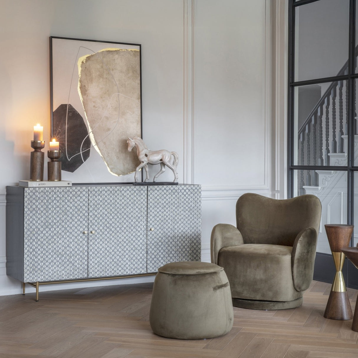 Libra Interiors Bingham green velvet swivel armchair with rounded back and curved arms, styled beside a patterned sideboard and matching footstool.