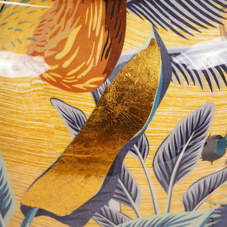 Close-up of Libra Interiors Painted Iron Jungle Planter in Gold, showing gold foil leaf detail amid blue tropical foliage on a yellow enamelled surface.