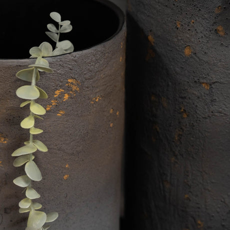 Close-up of Libra Interiors Textured Iron Cylinder Planters in mottled blue-grey with gold flecks, one holding a eucalyptus stem against the darker planter.