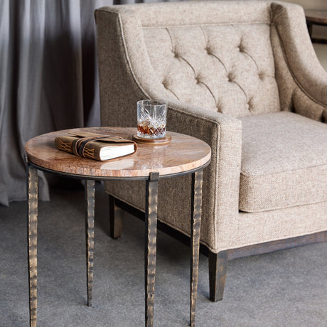 Libra Interiors Round Marble Hammered Iron Side Table in bronze beside a tufted beige armchair, holding a leather journal and crystal whisky glass.