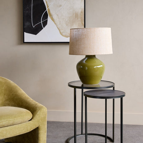 Libra Interiors Slate Effect Iron Nesting Side Tables in black holding a green ceramic lamp beside a chartreuse armchair and abstract wall art.